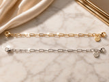 Gold and silver CharmFlip paperclip-link extender chains with lobster clasps on marble