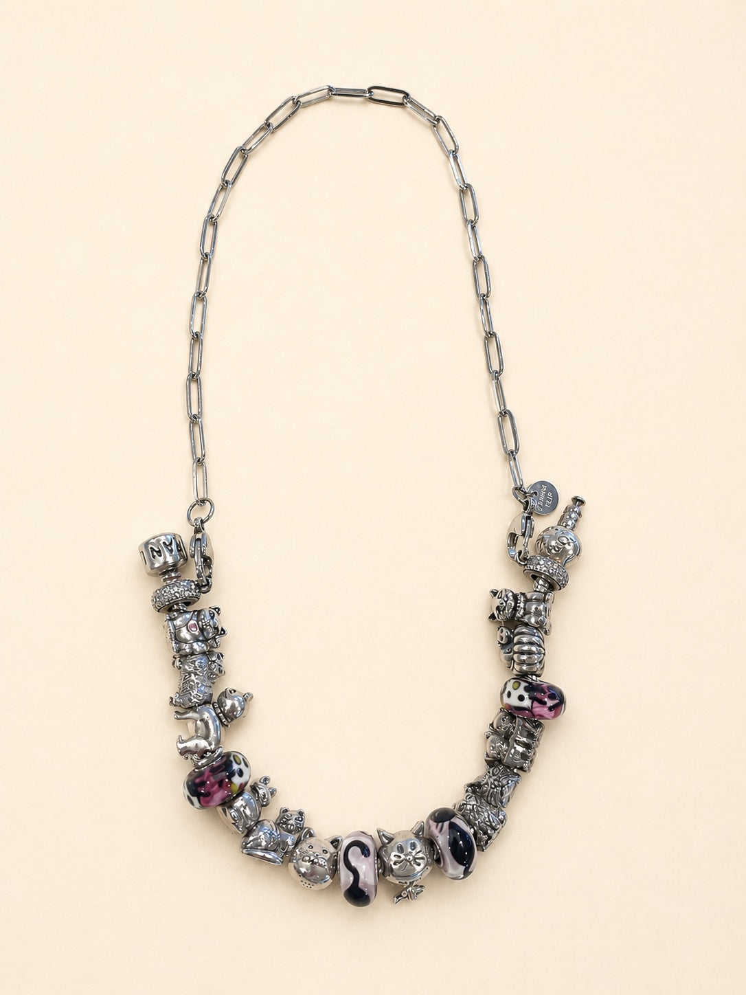 A charm bracelet worn as one continuous necklace on a CharmFlip paperclip chain, photographed on a cream background